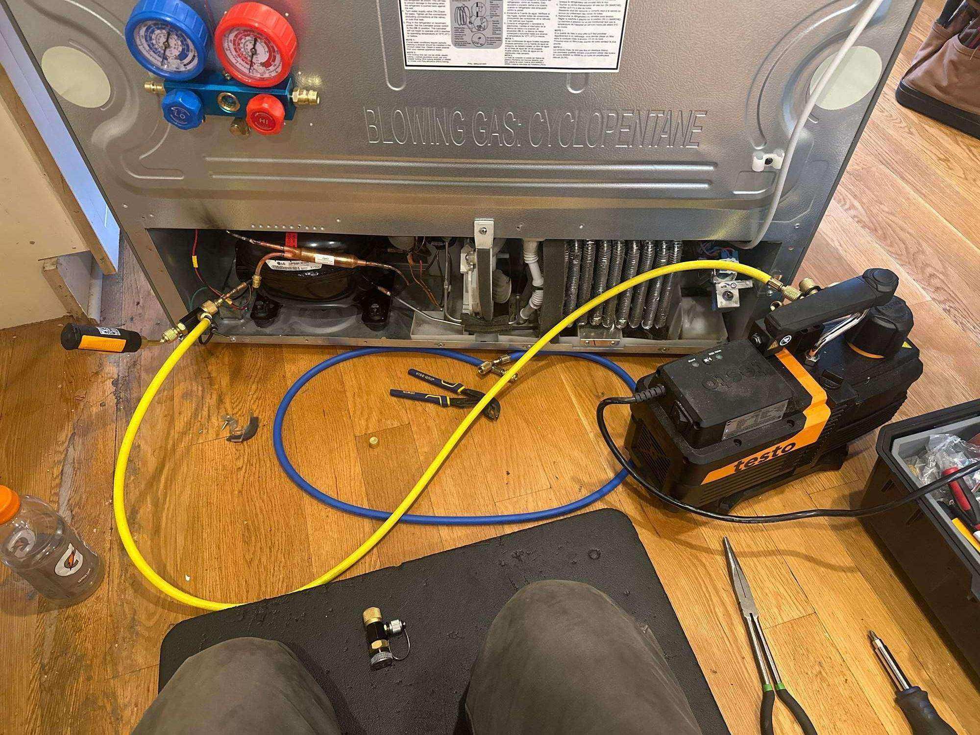 Refrigerator compressor being serviced with refrigerant gauges and recovery equipment